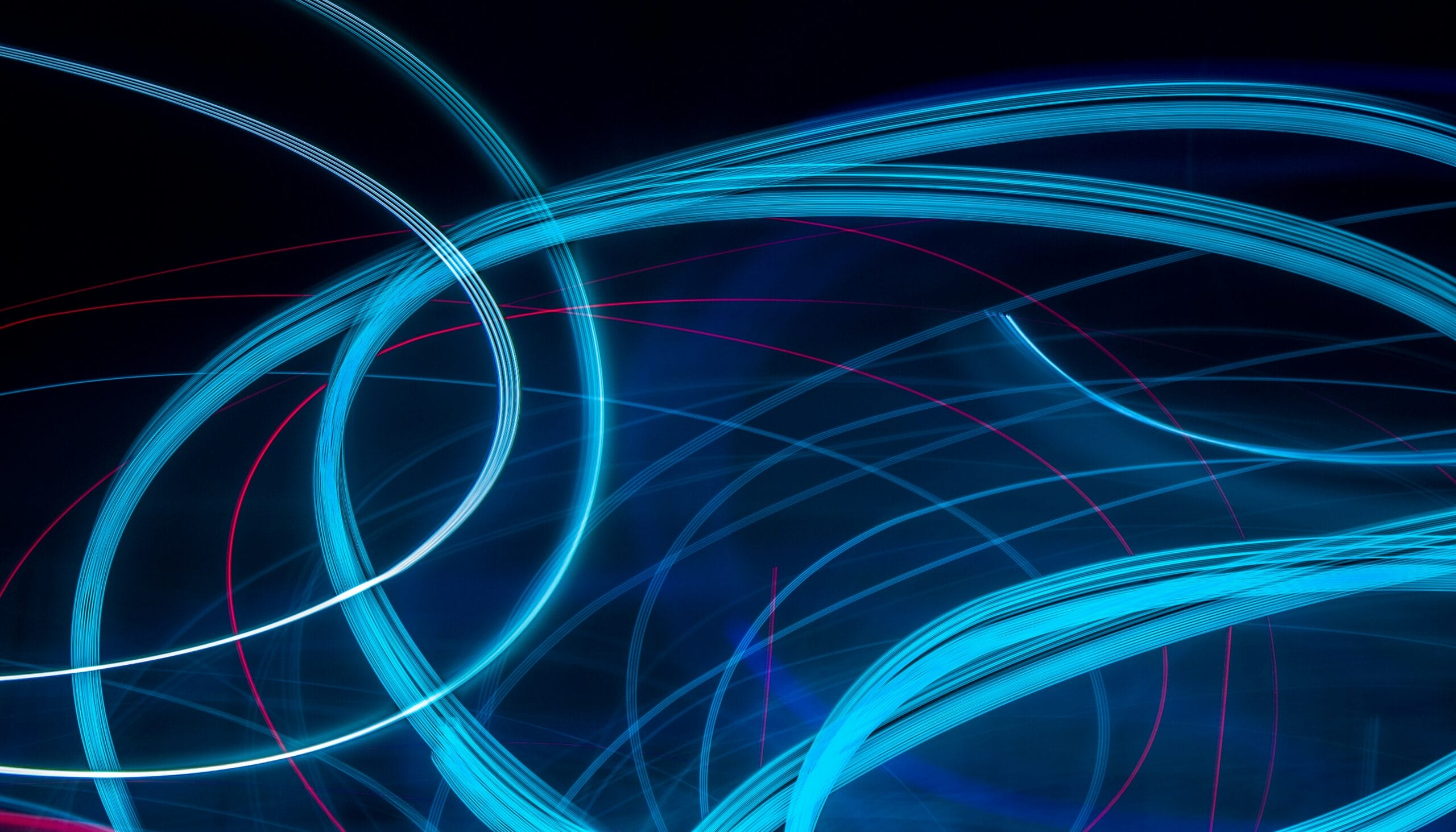 Abstract light trails in blue and pink against a dark background.