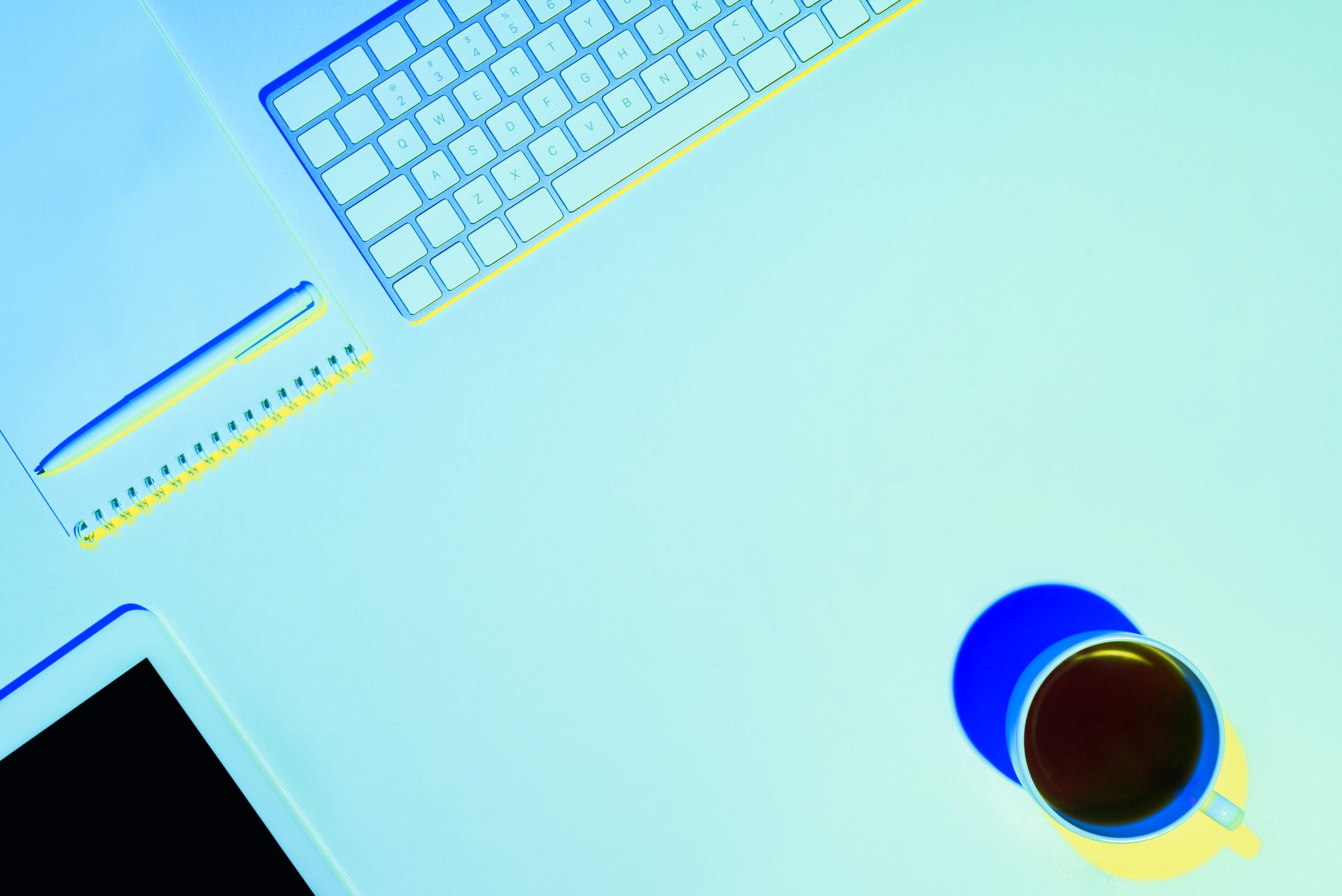 A minimalist workspace featuring a keyboard, notebook, pen, tablet, and a cup of coffee.