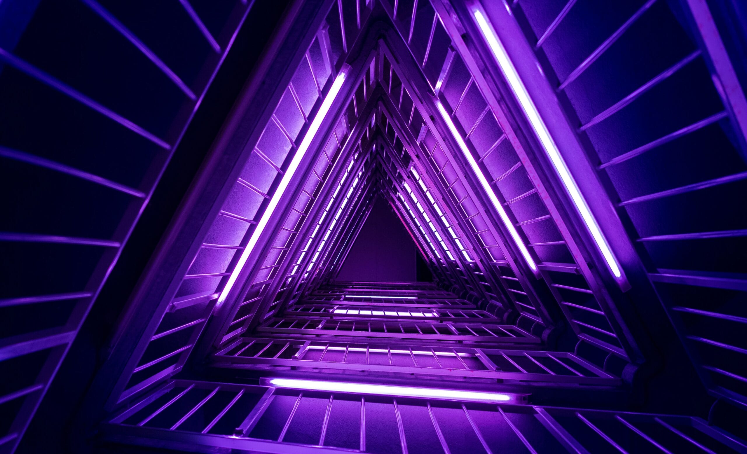 A geometric structure illuminated by vibrant purple lights, creating a triangular perspective.