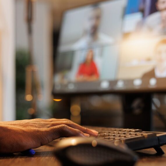 A person in a suit typing on a keyboard during a video conference call.