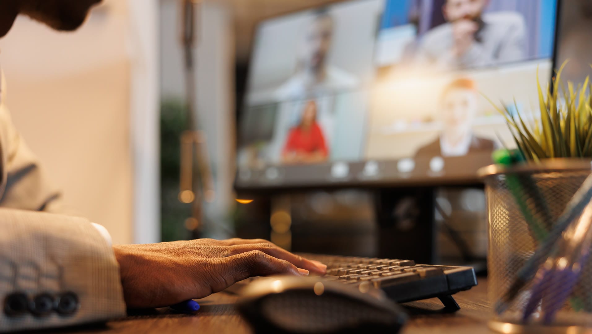 A person in a suit typing on a keyboard during a video conference call.