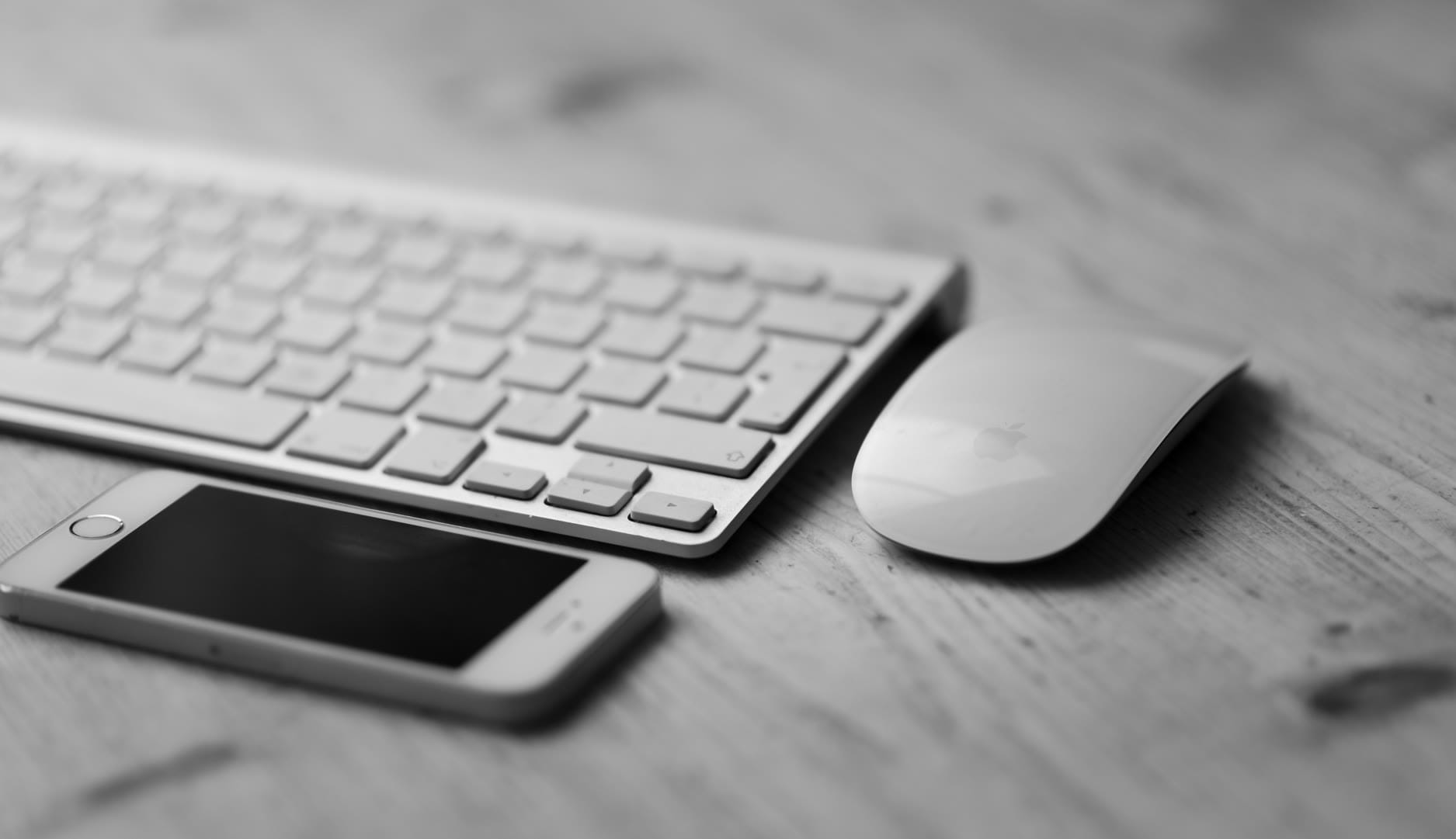 A minimalist workspace featuring a keyboard, mouse, and smartphone on a wooden surface.