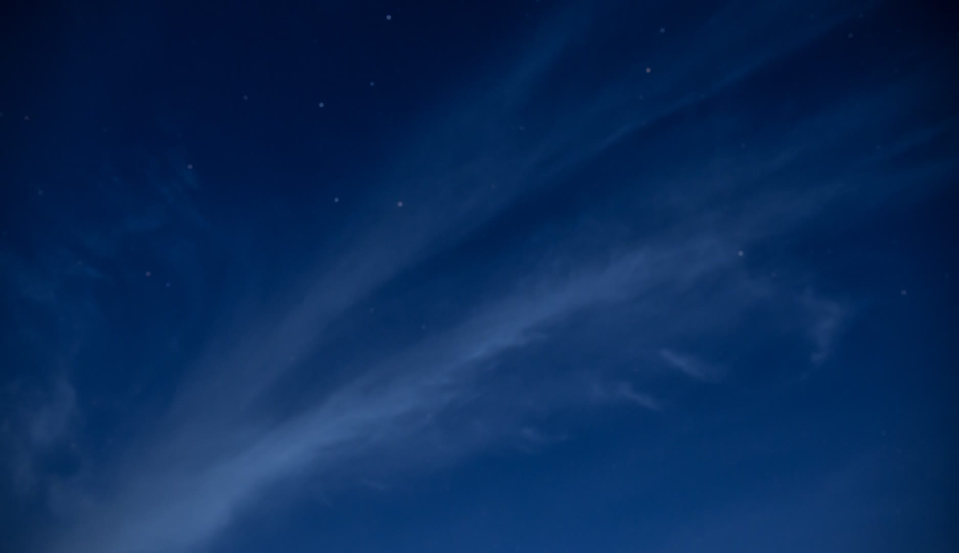 A night sky filled with stars and wispy clouds against a deep blue backdrop.
