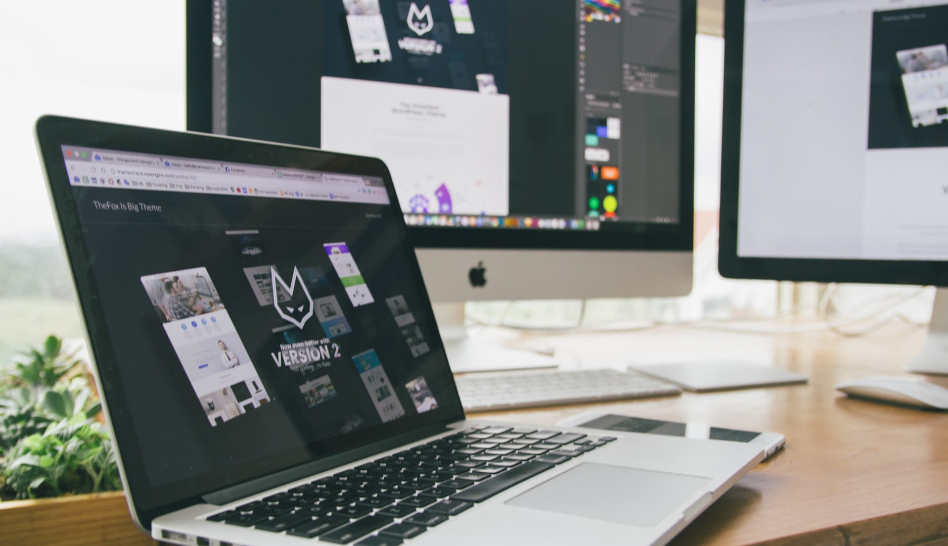 A workspace featuring a laptop and two monitors displaying web design projects.