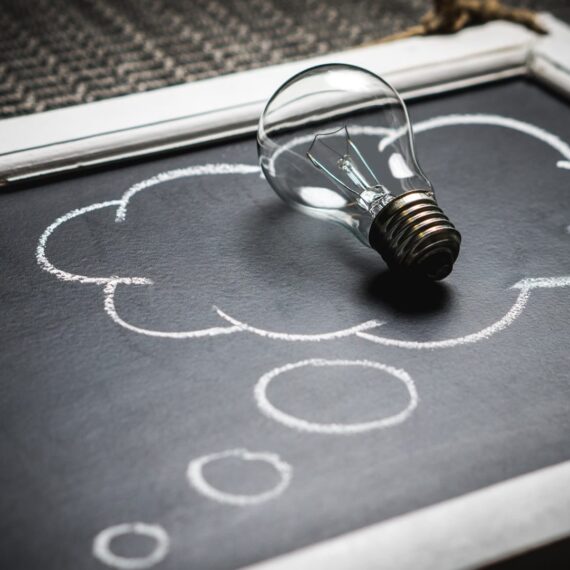 A light bulb placed on a chalkboard with drawn thought bubbles.
