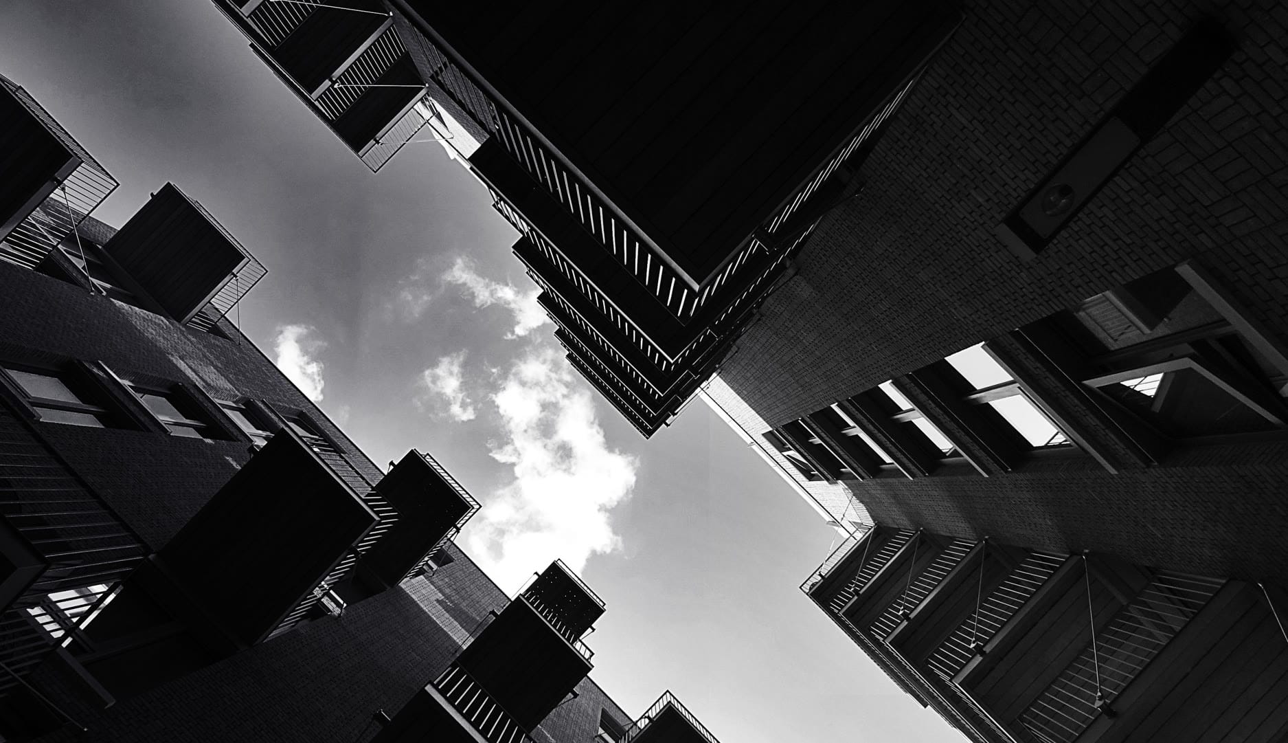 Looking up at modern buildings with geometric shapes against a cloudy sky.