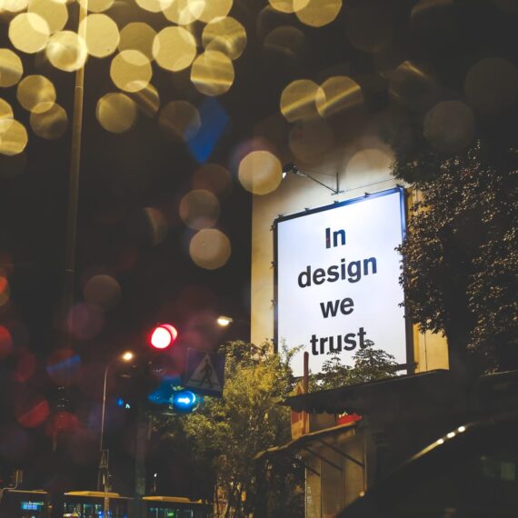 A nighttime city scene featuring a billboard with the text 'In design we trust.'