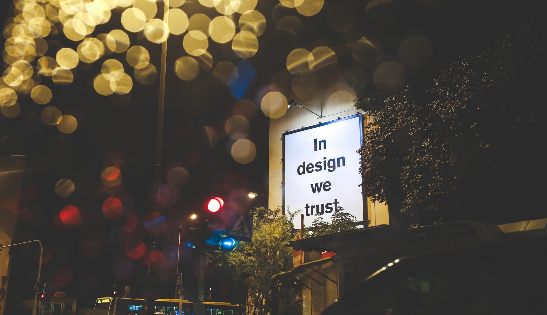 A nighttime city scene featuring a billboard with the text 'In design we trust.'
