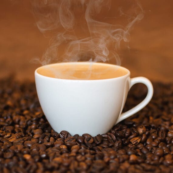 A steaming cup of coffee surrounded by roasted coffee beans.