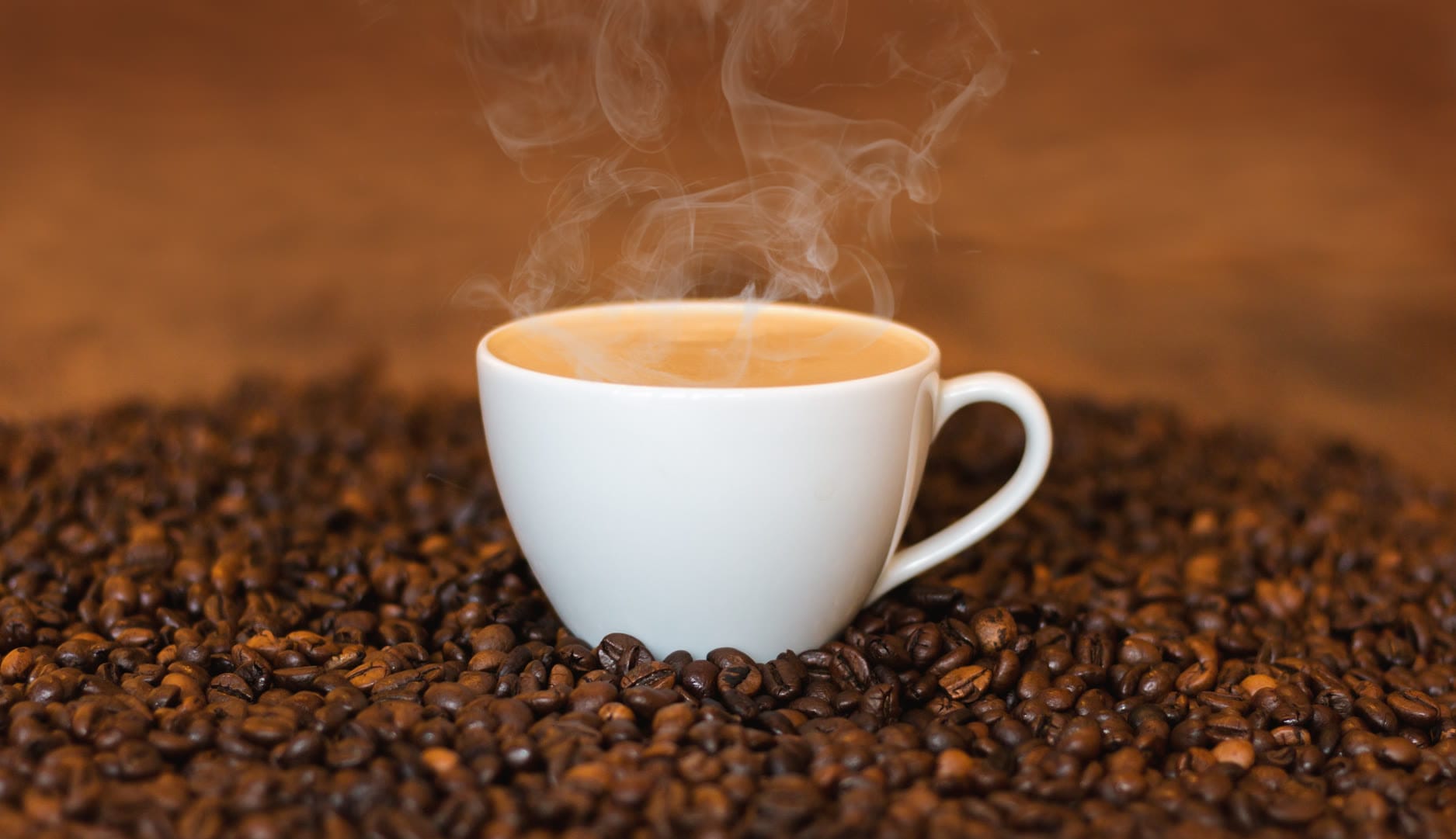 A steaming cup of coffee surrounded by roasted coffee beans.