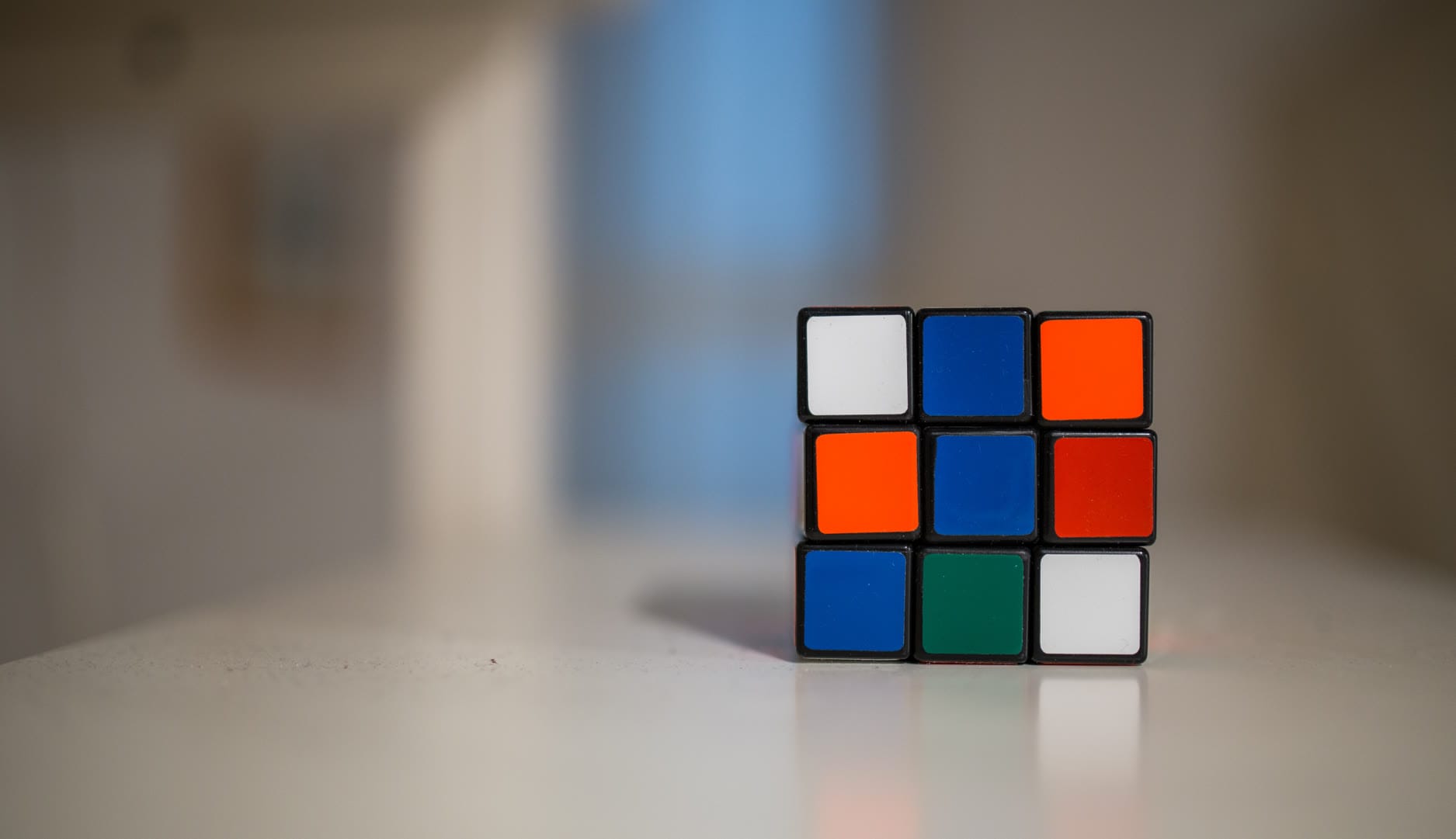 A partially solved Rubik's Cube on a white surface with a blurred background.