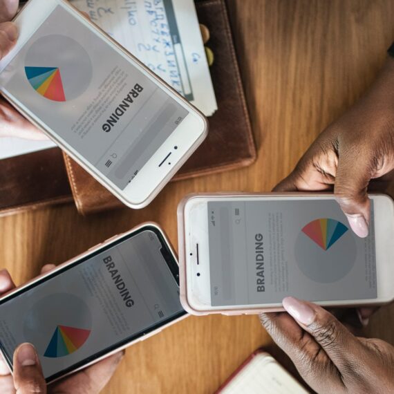 Three hands holding smartphones displaying branding pie charts on a wooden table.