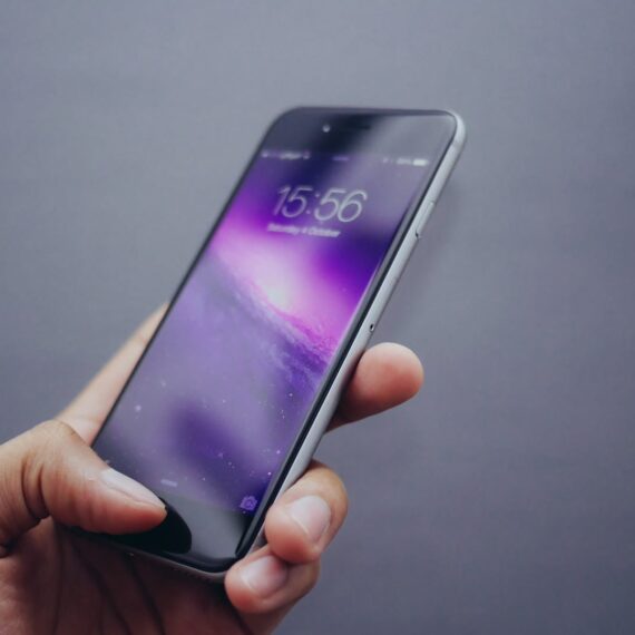 A hand holding a smartphone displaying a vibrant purple wallpaper.