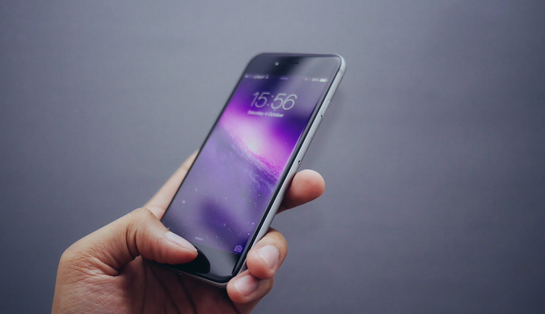 A hand holding a smartphone displaying a vibrant purple wallpaper.