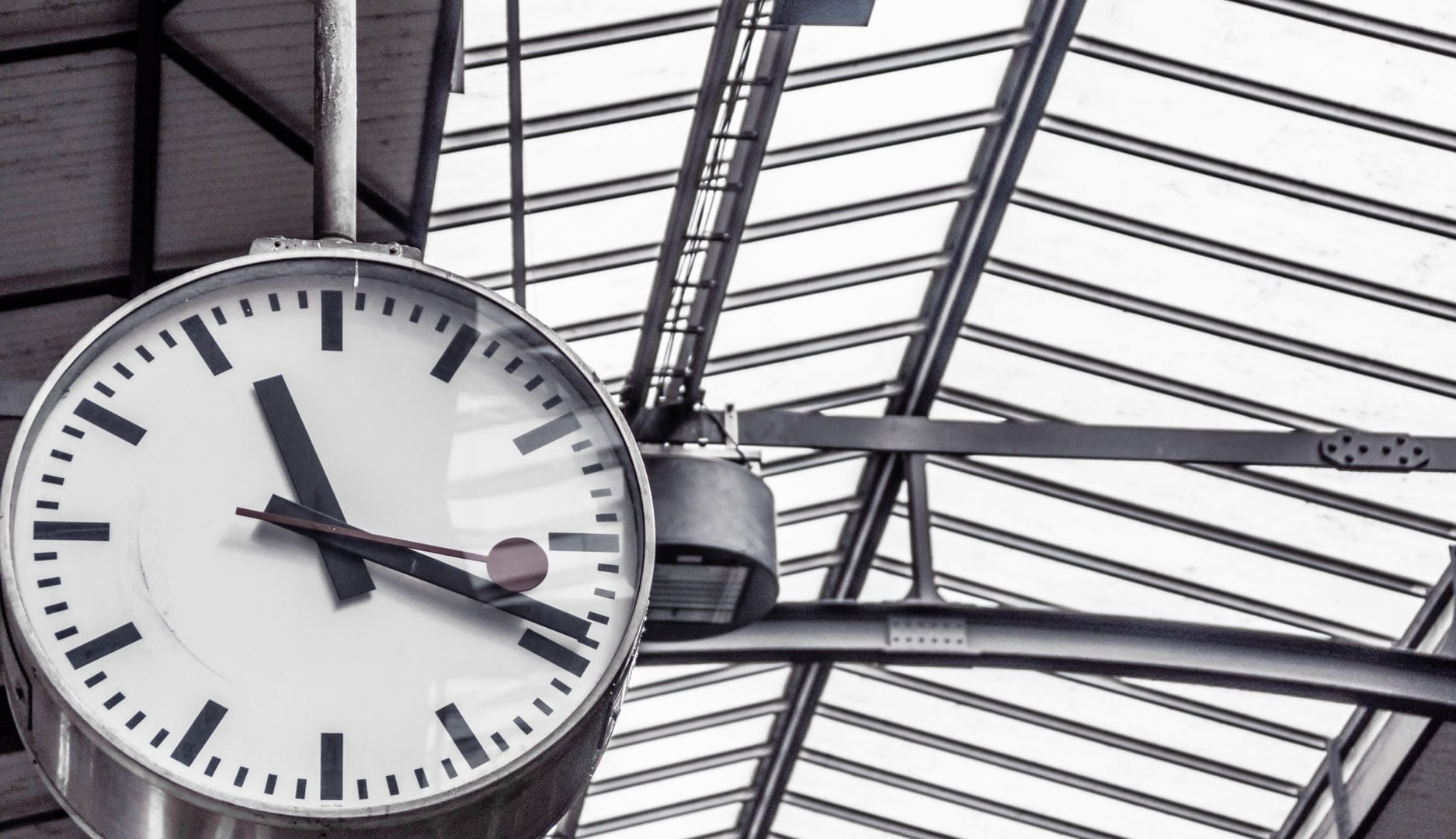 A large round clock hanging in a modern train station.