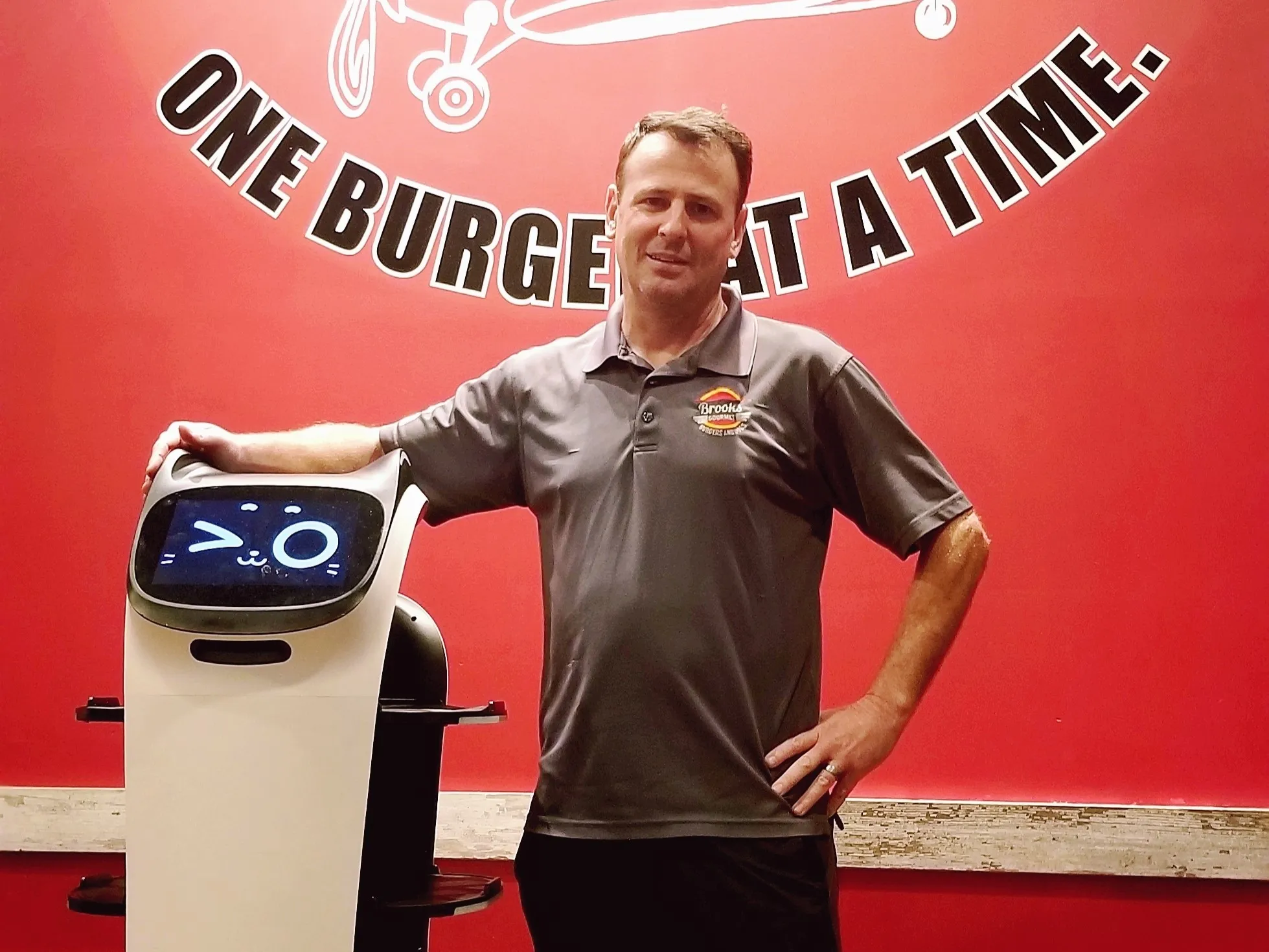 A man, Todd Brooks owner of Brooks Burgers, the #2 burger joint in the USA, stands next to a robot in a burger restaurant that we designed their website and digital marketing strategy.
